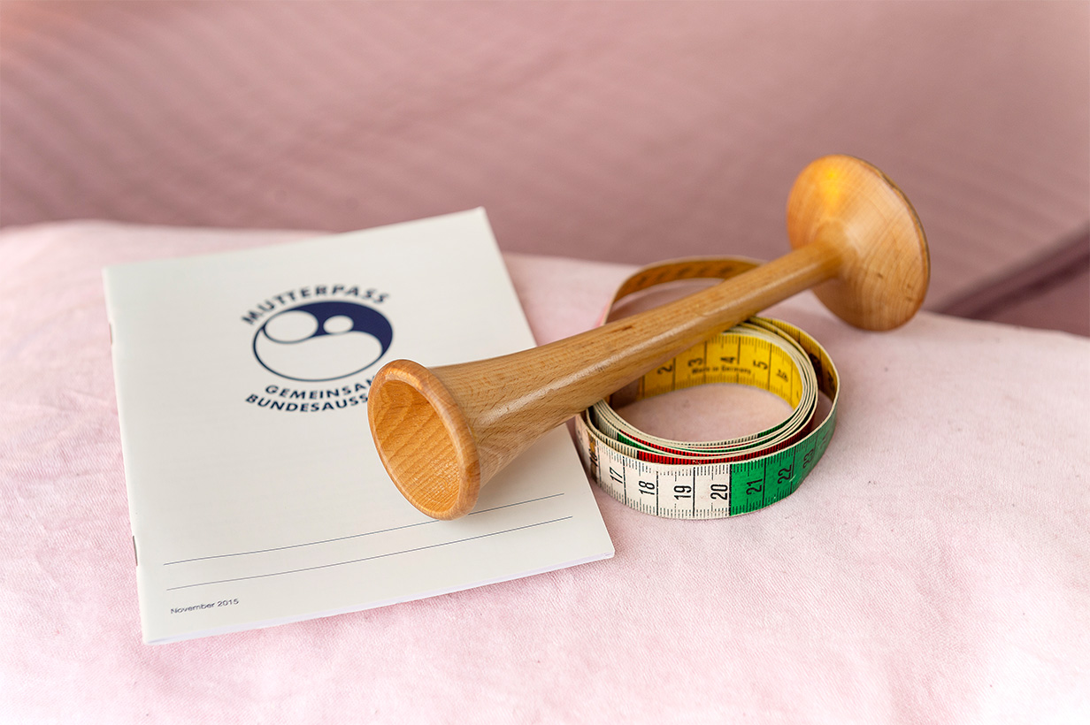 Mutterpass, Maßband, Pinar-Rohr liegen auf rosaner Fläche